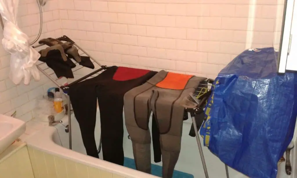 wetsuits hanging on a laundry rack in a bath