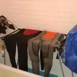 wetsuits hanging on a laundry rack in a bath
