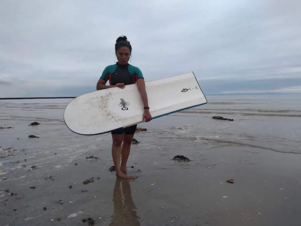 my wife with my finless surfboard standing on the beach