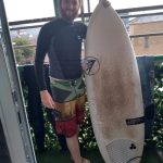 surfer in boardshorts with wetsuit top and surfboard